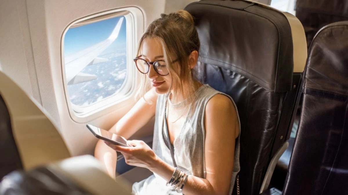 A female passenger on a flight uses her smartphone while the plane is flying.